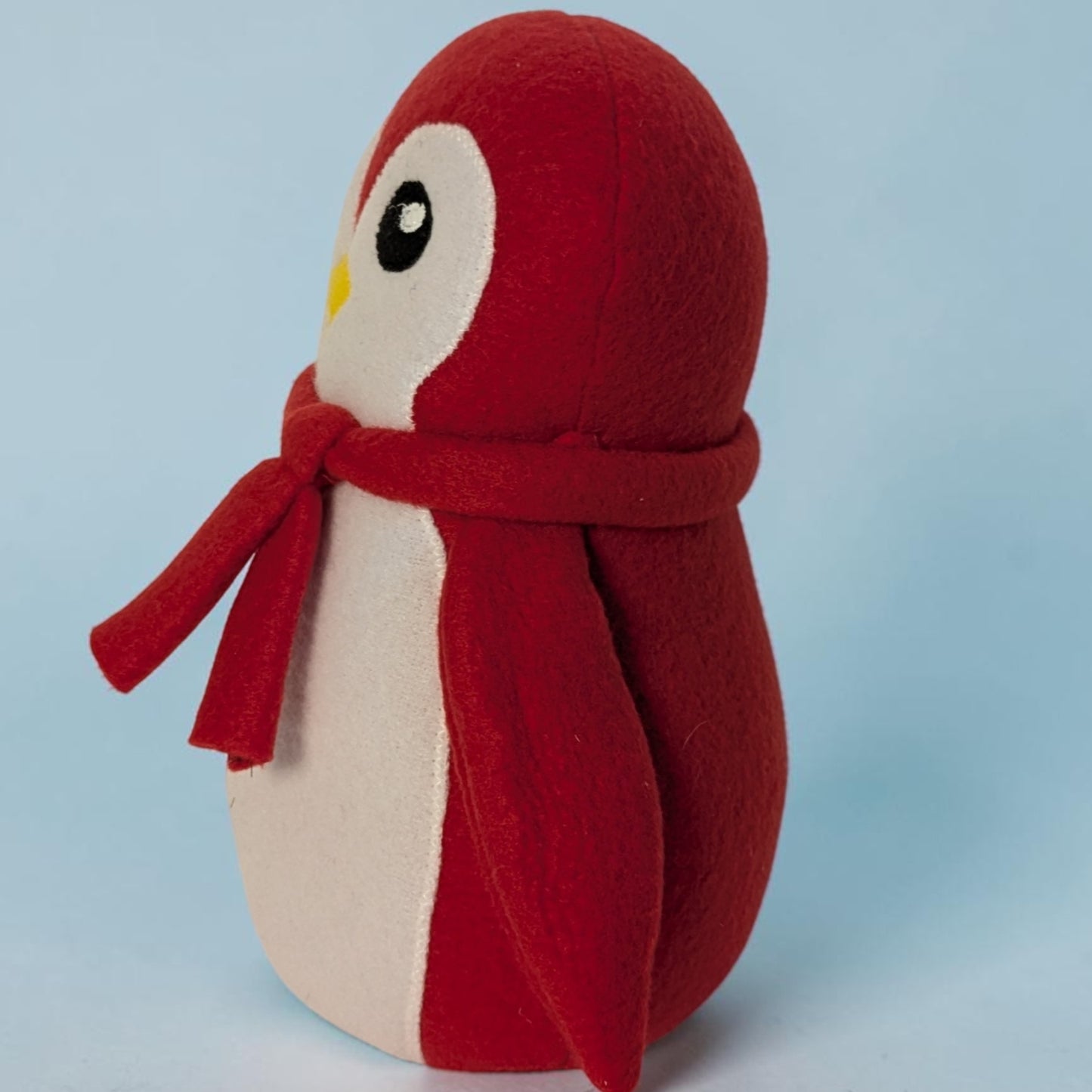 A red and white plush penguin toy wearing a matching red scarf, photographed against a light blue studio background.